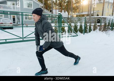 Un uomo di mezza età fa affondamenti e le gambe si allungano all'aperto. Si riscalda quando fa freddo, preparando la parte inferiore del corpo per una corsa. Foto Stock