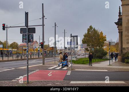 Pista ciclabile rossa con attraversamento zebra a Goerdelerring a Lipsia in autunno; traffico urbano con auto, ciclisti e pedoni al semaforo Foto Stock