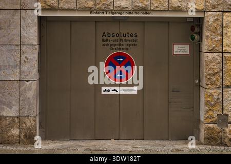 Porta di un garage in metallo di un parcheggio sotterraneo a Lipsia con cartelli "No stop" e avviso di traino su una facciata in pietra in Sassonia, Germania Foto Stock