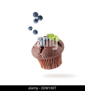 Muffin singolo al cioccolato appena sfornato con mirtilli e foglie di menta che volano su sfondo bianco. Dolce cupcake che cade. Carta di pasticceria con copia spp Foto Stock