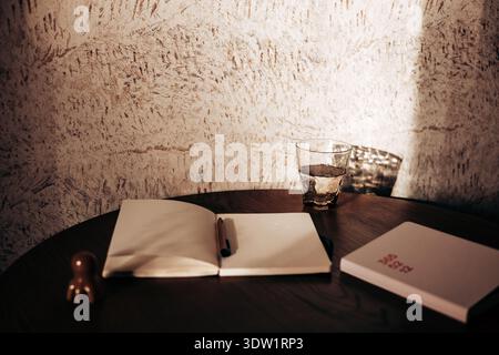Spazio di lavoro minimalista con notebook aperto su un tavolo in legno, bicchiere d'acqua e pianificatore con calda luce naturale. Atmosfera tranquilla, ombre morbide, texture Foto Stock