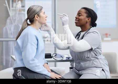 Donna caucasica di mezza età sottoposta a esame oculare da parte di Black Female Doctor Foto Stock