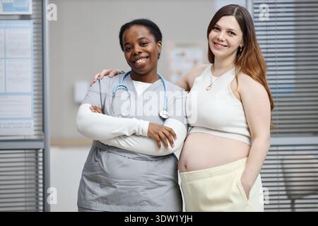Giovane donna incinta caucasica in piedi con sorridente Nera infermiera Foto Stock