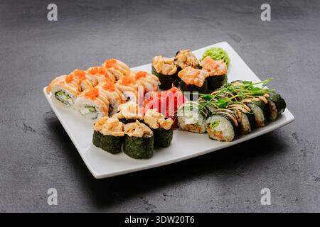 Sushi roll assortiti con condimenti di pesce serviti su piatti bianchi di cucina giapponese Foto Stock