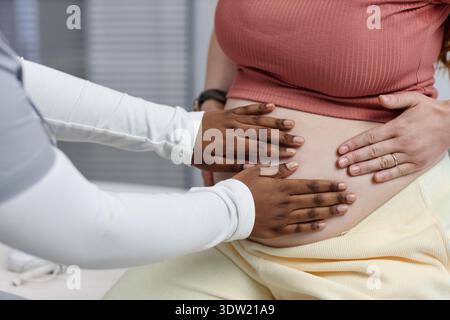 Giovane donna incinta caucasica esaminata da lavoratore sanitario femminile di colore Foto Stock