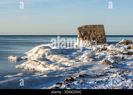 Mare invernale con spesse formazioni di ghiaccio che circondano le rovine della storica fortezza costiera sulla riva del Mar Baltico a Liepaja, Lettonia Foto Stock