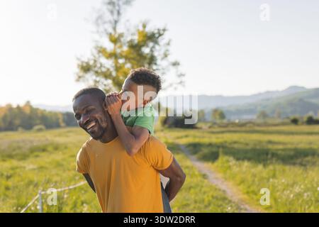 Padre e figlio che sussurrano condividono un momento felice all'aperto durante il tramonto, godendosi un'interazione giocosa in natura. Foto Stock