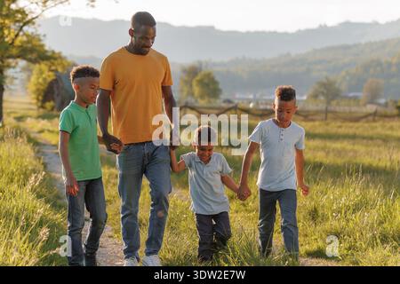 Un padre single ama passeggiare all'aperto con i suoi tre figli, condividendo momenti felici tenendo per mano e ridendo. Foto Stock