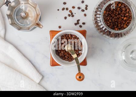 Un macinacaffè manuale, una caffettiera e un vasetto di chicchi di caffè tostati. Vista dall'alto del tavolo in marmo Foto Stock