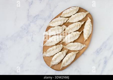 Gyoza crudi su un asse di legno. Messa a fuoco selettiva, vista dall'alto Foto Stock