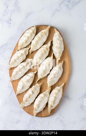 Gyoza crudi su un asse di legno. Messa a fuoco selettiva, vista dall'alto Foto Stock