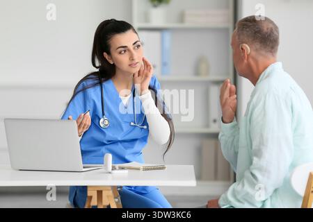 Uomo maturo con l'apparecchio acustico visita medico al tavolo in clinica Foto Stock