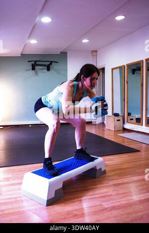 Donna che esegue gli squat con i manubri sul passo aerobico Foto Stock