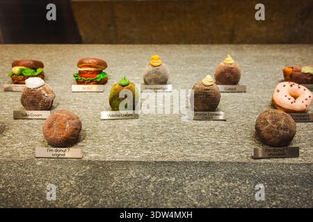 New York, USA, 1 novembre 2025: Ciambelle mochi gourmet assortite e sapori creativi di dessert esposti sul bancone della panetteria in un moderno bar interno Foto Stock