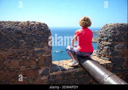 Donna anziana seduta su una pistola sulla fortezza di Capo Verde Foto Stock