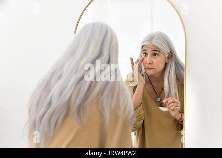 Donna matura che si tocca la faccia, si impegna nella routine di autocura Foto Stock