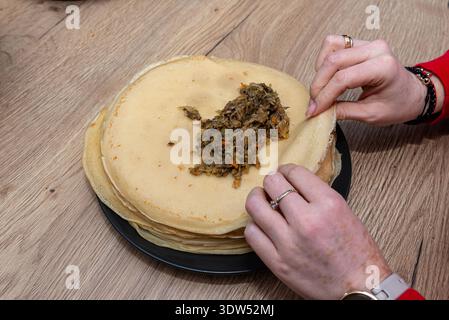 Mani di donna che riempiono crepes con un saporito cavolo e farcitura di funghi su un tavolo di legno Foto Stock