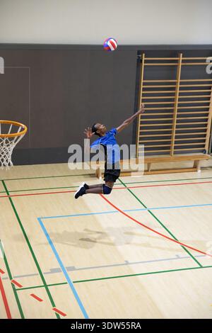Giovanissimo afroamericano che salta con una maglia blu-rossa-bianca-blu sul campo da palestra Foto Stock