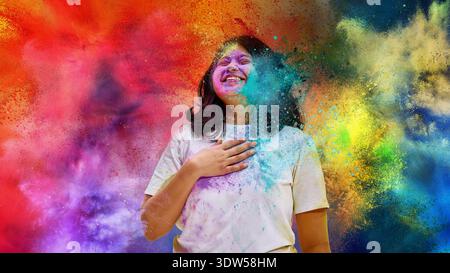 Donna che ride con la mano sul petto durante l'esplosione del colore Holi Foto Stock