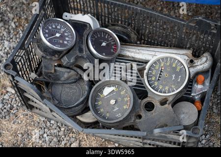 Vista ad angolo alto di una cassa in plastica riempita con parti di auto d'epoca, tra cui tachimetri, indicatori e componenti meccanici in un veicolo all'aperto Foto Stock