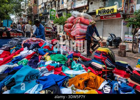 Mercato di strada a Chandni Chowk, Vecchia Delhi. Un uomo fa un giro in risciò carico di sacchi e passa davanti a bancarelle di vestiti colorati. Nuova Delhi, capitale nazionale, Terri Foto Stock