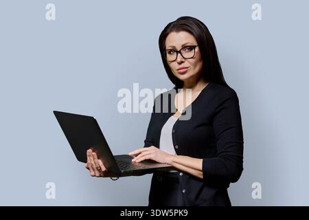 Ritratto di donna matura con laptop su sfondo grigio Foto Stock