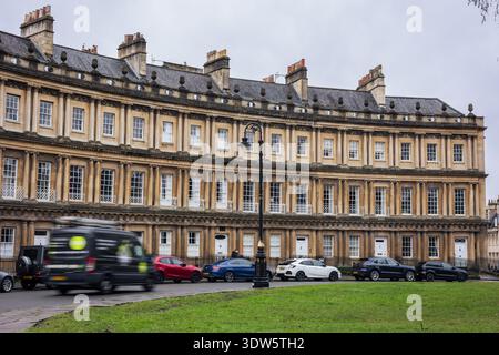 Il Circo di Bath, iconiche case cittadine georgiane circolari con facciate dettagliate e camini sotto un cielo nuvoloso, prato verde in primo piano Foto Stock
