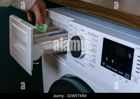 Primo piano di una persona che inserisce una cialda di detergente nel cassetto della lavatrice. Foto Stock