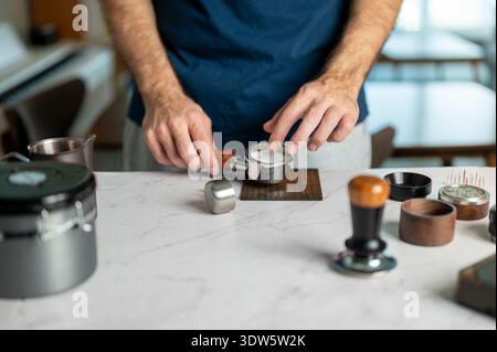Un barista esperto che utilizza un filtro di carta sul caffè macinato perfettamente nel portafiltro, mostrando l'arte della preparazione dell'espresso in un ambiente accogliente Foto Stock