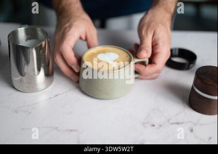 Un barista esperto versa meticolosamente il latte in una tazza, creando una squisita latte art a forma di cuore, che mostra l'arte coinvolta nelle pubbliche relazioni del caffè a casa Foto Stock