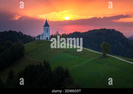 Vista aerea di una famosa chiesa di Jamnik arroccata sulla cima di una vibrante collina verde sotto una tenda da tramonto, Jamnik, Slovenia. Foto Stock
