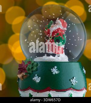 Babbo Natale in un globo innevato con pezzi bianchi che galleggiano nell'acqua con luci natalizie dorate e gialle che si illuminano alle spalle. Foto Stock