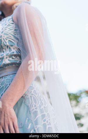 Una donna indossa un abito blu con un colletto in pizzo bianco. Lei è in piedi di fronte a un cielo blu Foto Stock