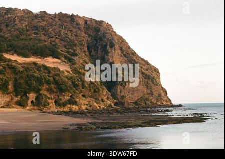Paesaggio marino panoramico caratterizzato da un'aspra scogliera costiera, costa rocciosa e acqua calma durante la calda luce dell'ora d'oro. Foto Stock