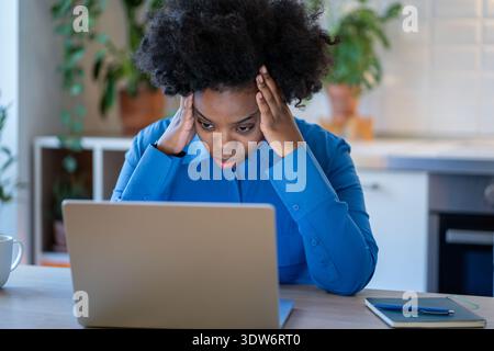 Stanchezza cronica. Stanca e distratta donna nera a casa sopraffatta guardando un notebook. Sovraccarico di lavoro a distanza femminile afroamericana stressato. Foto Stock
