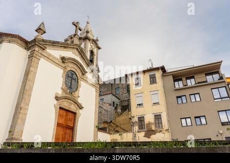 Vista di una chiesa storica con dettagli in pietra accanto a edifici residenziali di epoca antica a Porto, Portogallo, che mostrano una miscela di architettura tradizionale e Foto Stock