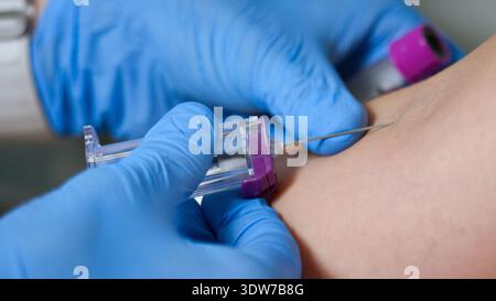 Un operatore sanitario sta prelevando sangue da un braccio di pazienti utilizzando un ago e una provetta in un ambiente clinico sterile. Foto Stock