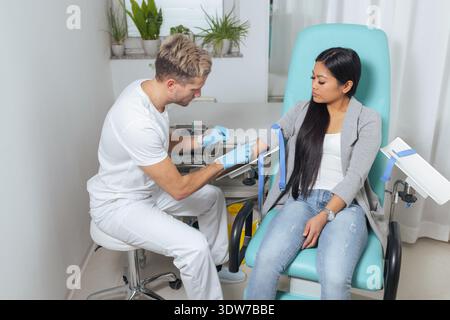 Il lavoratore aspira il sangue dal braccio dei pazienti in un ambiente medico sterile utilizzando attrezzature e tecniche moderne per i test. Foto Stock