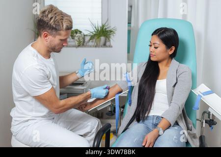Un operatore sanitario sta prelevando un campione di sangue da un braccio di pazienti in una clinica medica. L'impostazione è pulita e sterile. Foto Stock