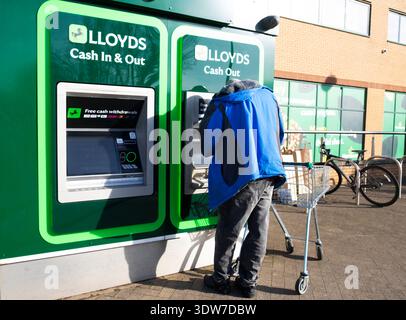 Vista posteriore di un uomo più anziano in piedi fuori dal supermercato Morrisons usando soldi prelevati dal bancomat della Lloyds Bank Regno Unito KATHY DEWITT Foto Stock