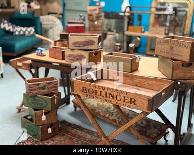 Interni di antiquariato vintage con casse in legno impilate e contenitori retrò disposti su tavoli da esposizione. Foto Stock