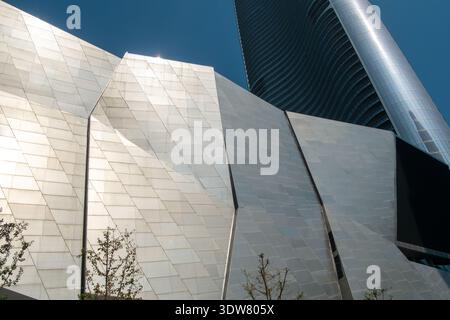 Primo piano orizzontale delle pareti esterne sfaccettate di un edificio moderno, focalizzato sulla superficie lucida e gli angoli geometrici che riflettono la luce solare brillante. Foto Stock