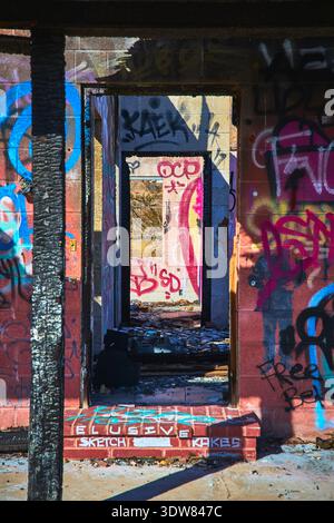 Porta coperta da graffiti e rovine nell'edificio abbandonato con detriti illuminati dal sole Foto Stock