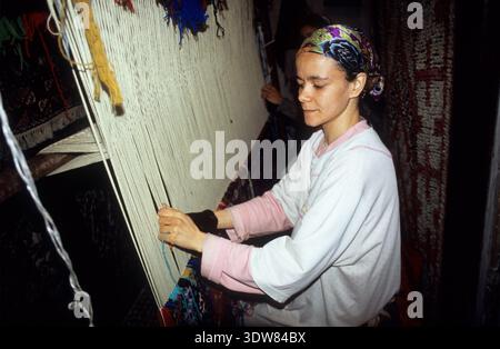 Una donna artigiana che fila manualmente il filato di lana su un grande telaio verticale per tessere un tappeto tradizionale in un laboratorio a Fez, Marocco. Foto Stock