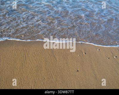 Le onde dell'oceano si infrangono su una spiaggia di sabbia liscia. Struttura naturale del mare e rilassante sfondo costiero con riflessi della luce del sole. Foto Stock