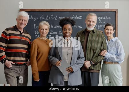 Diversi insegnanti di mezza età e senior che si mettono insieme in posa in aula Foto Stock