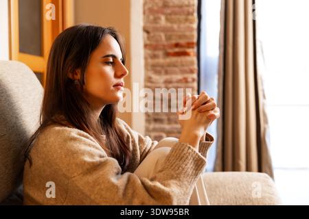 Donna che prega con le mani agganciate che sembra sperando Foto Stock