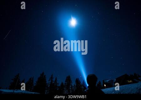 Una persona è in piedi nella neve con una torcia, guardando il cielo. Il cielo è pieno di stelle e di una luna luminosa. La scena ha un pacifico Foto Stock