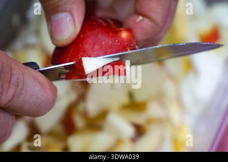 Primo piano della mela rossa affettata a mano con un coltello sul tavolo da cucina. Foto Stock