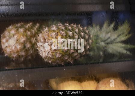 Due ananas interi appoggiati sullo scaffale in un'esposizione di prodotti alimentari bui. frutta tropicale fresca, matura e dalla consistenza piccante e dal sapore dolce per una dieta sana e sana Foto Stock